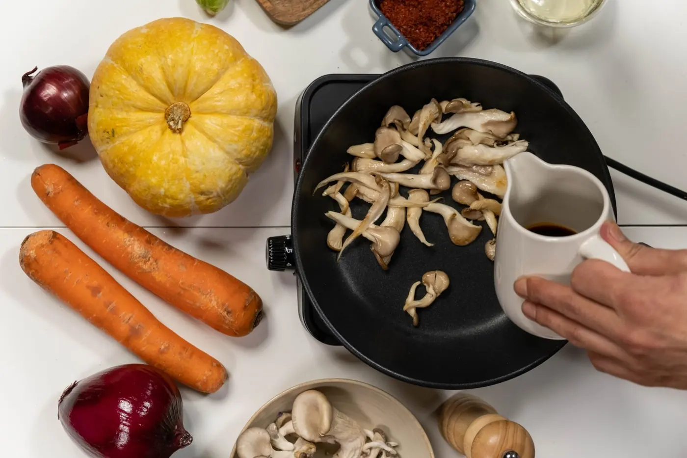 Austernpilze braten in einer schwarzen Pfanne, daneben Herbstgemüse