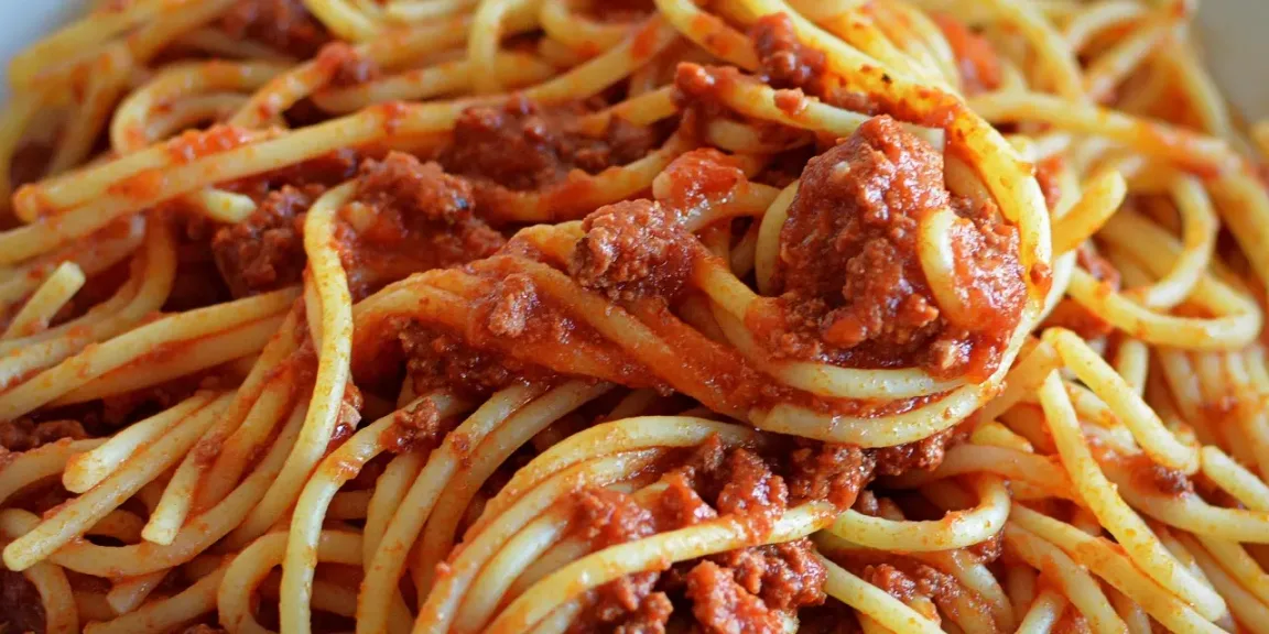 Eine Nahaufnahme zeigt Spaghetti, die mit roter Tomatensauce und krümeligem Hackfleisch vermischt sind.