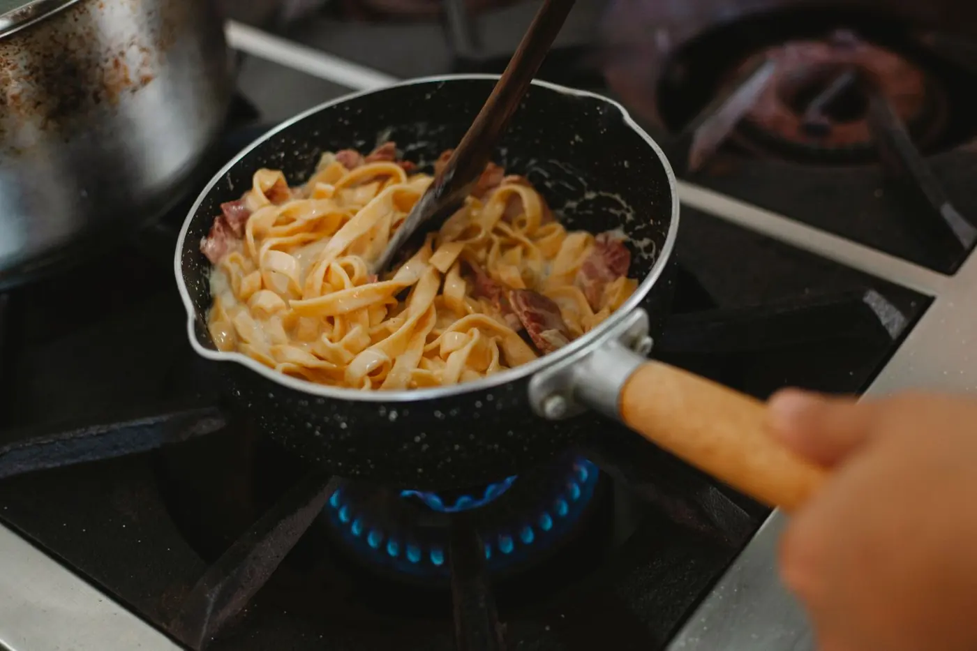 Pfanne mit Pasta über blauer Gasflamme