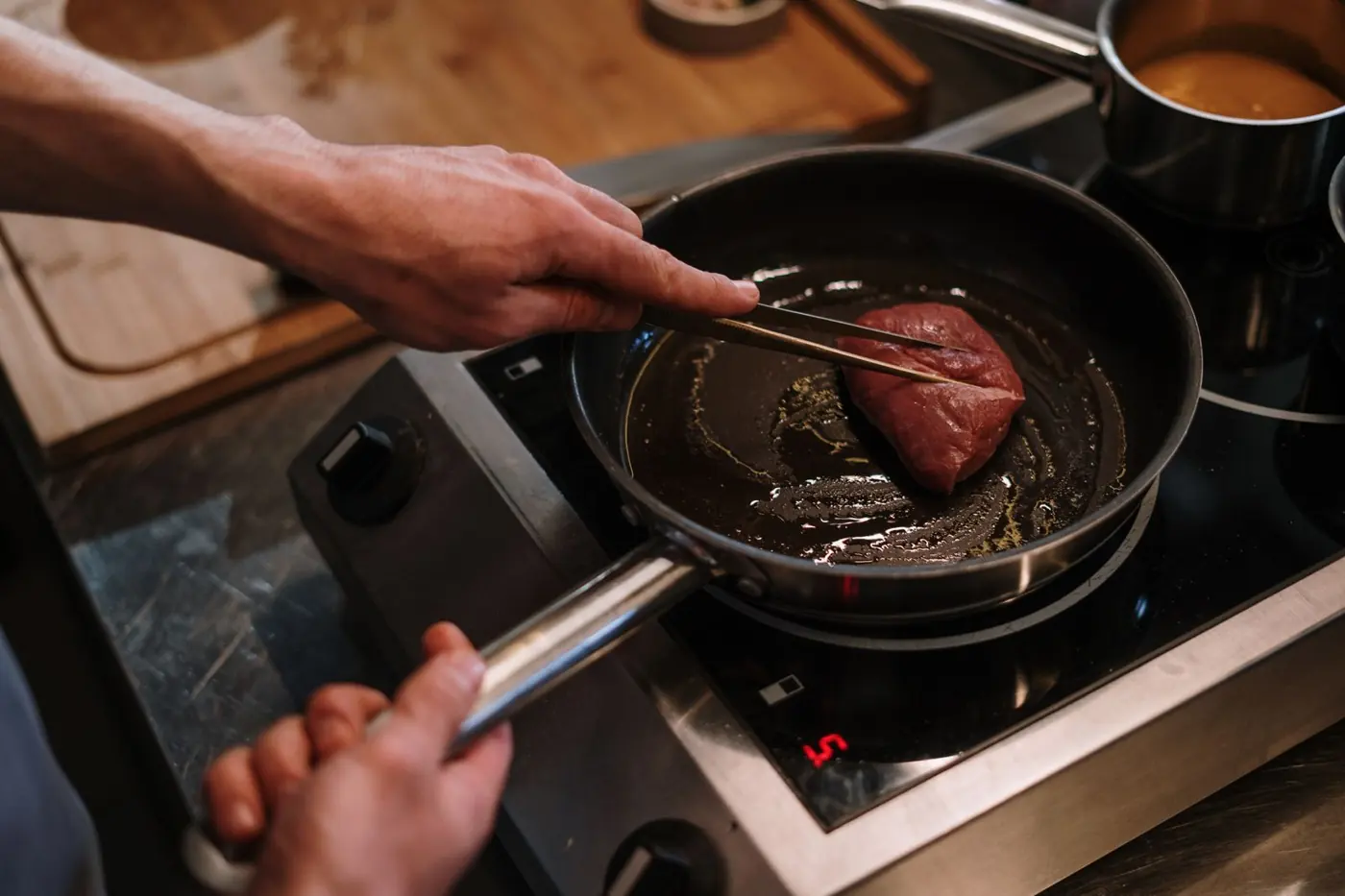 Steak wird mit der Zange in die heiße Pfanne gelegt