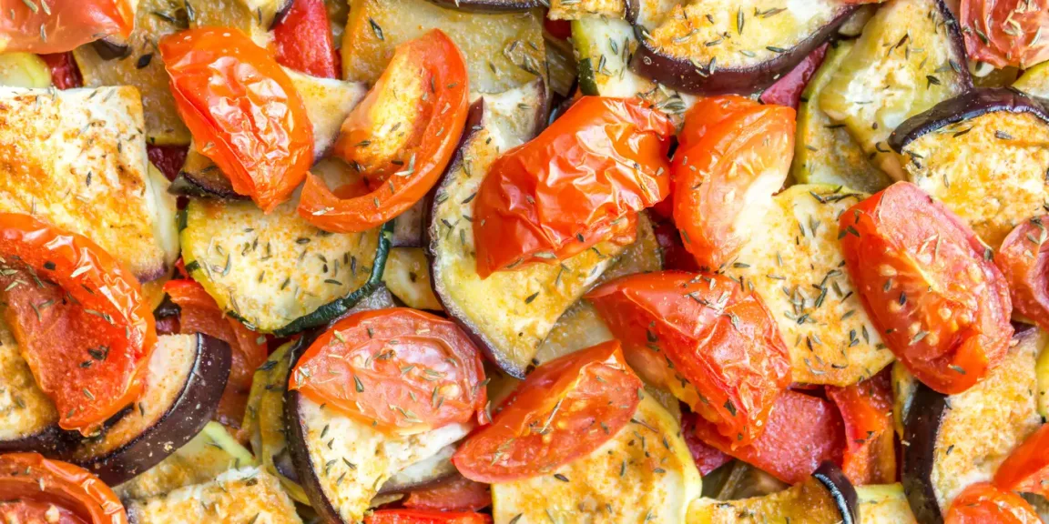Zu sehen ist eine Nahaufnahme von gebackenem Ofengemüse mit Tomaten-, Zucchini-, Auberginen- und weiteren Gemüsestücken, die mit Kräutern bestreut sind.