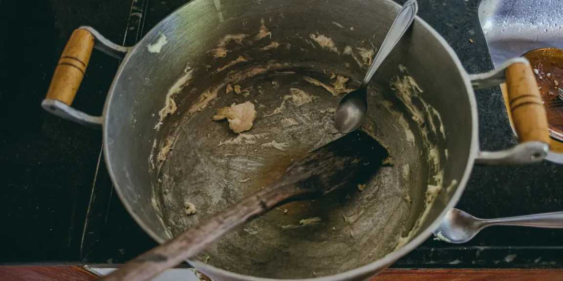 Reste einer hellen Mehlschwitze am Boden eines Kochtopfs mit Löffel und Holzlöffel