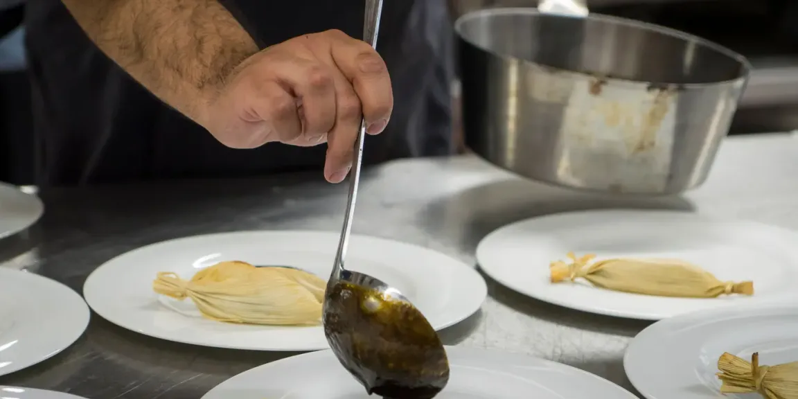 Koch gibt mit der Kelle dunkle Soße über eine angerichtete Tamale auf dem Teller