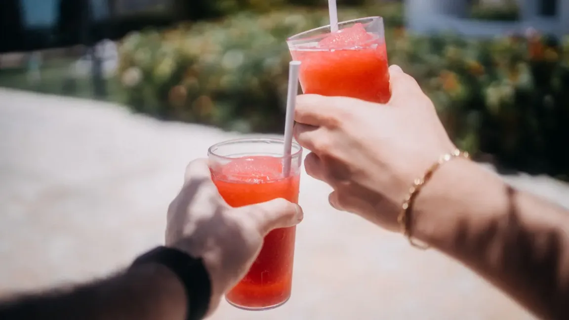 Zwei Personen halten im Freien jeweils ein durchsichtiges Glas mit rotem, körnig gefrorenem Slush-Getränk und Strohhalm in den Händen.