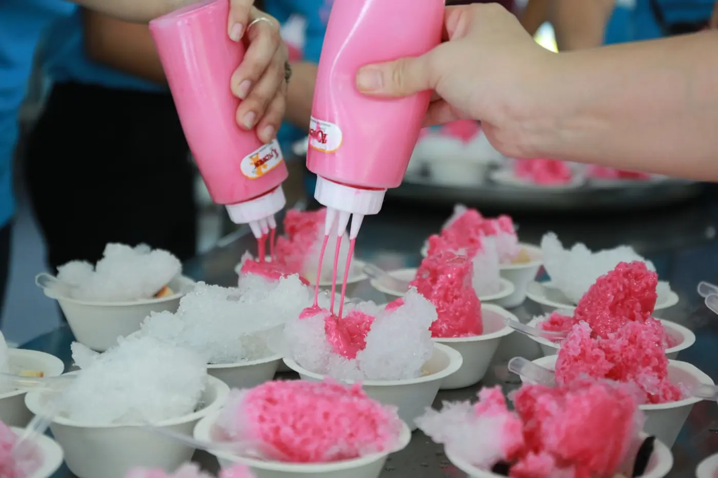 Sirup wird aus Quetschflaschen über gecrushtes Eis gegossen